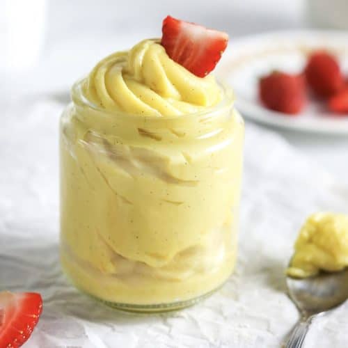 A clear jar full of pastry cream topped with a strawberry