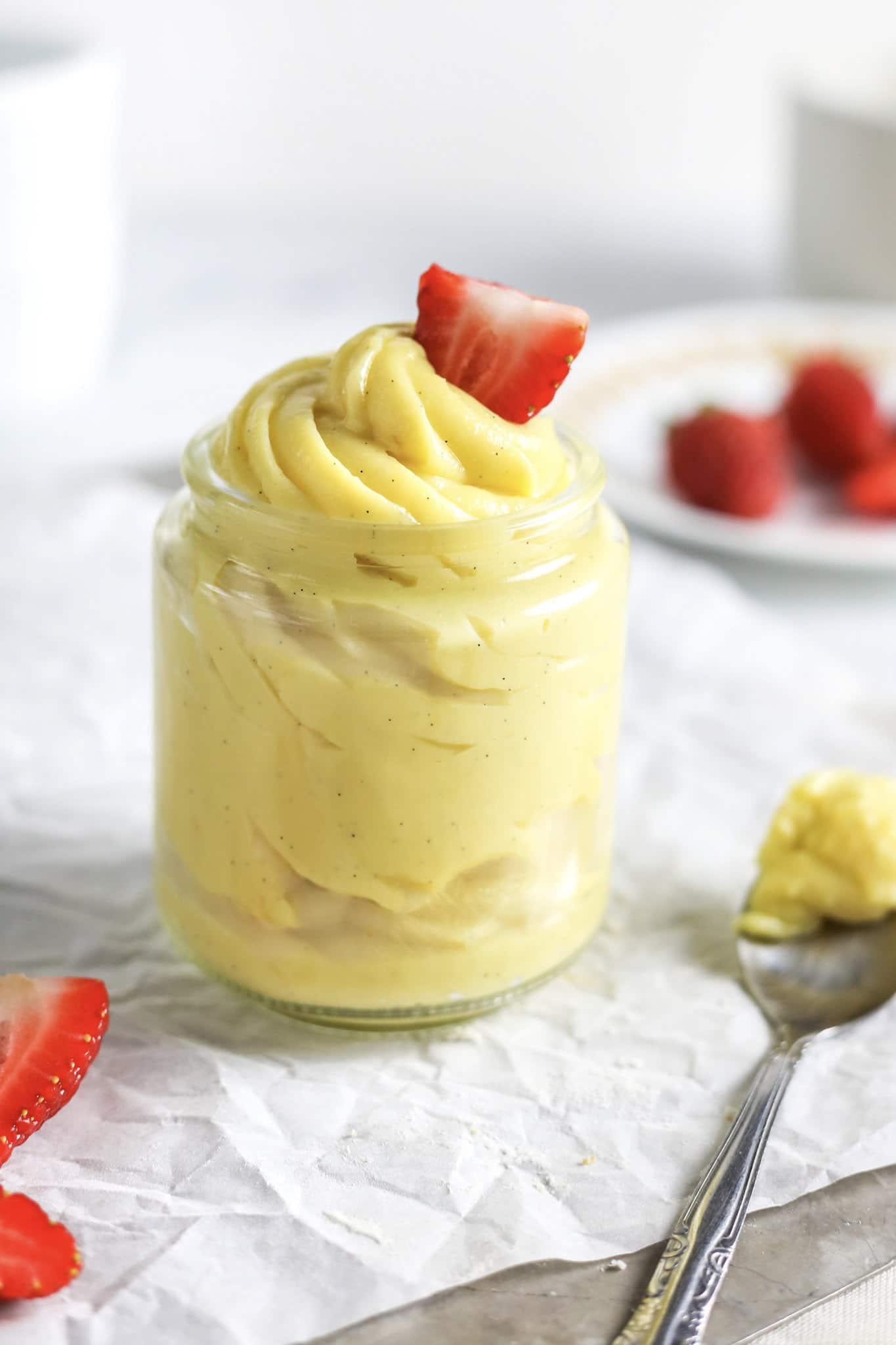 A clear jar full of pastry cream topped with a strawberry