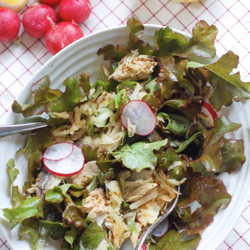 A bowl of mackerel salad with radishes and Lemons in background