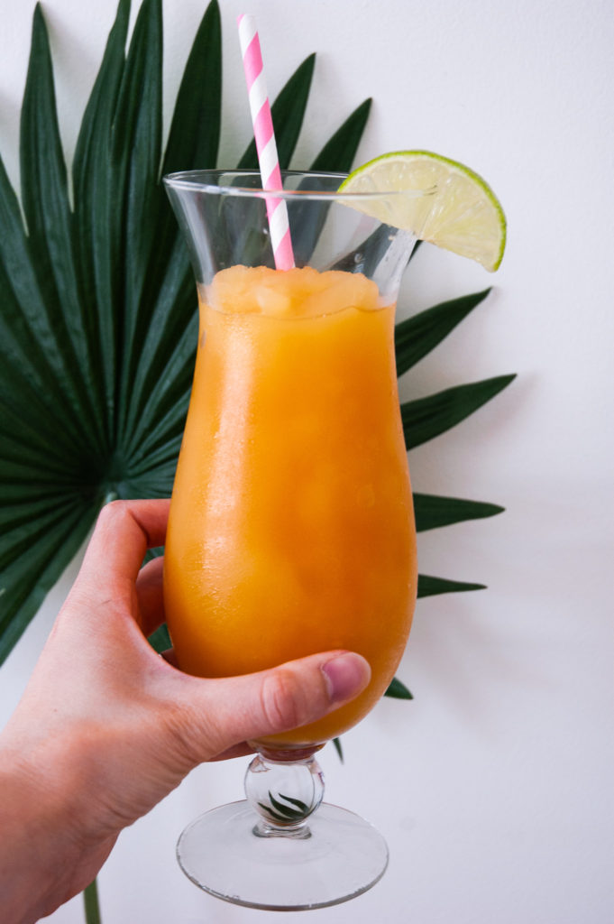 A hand holds the Pineapple and Orange Rum Slush in front of a palm leaf