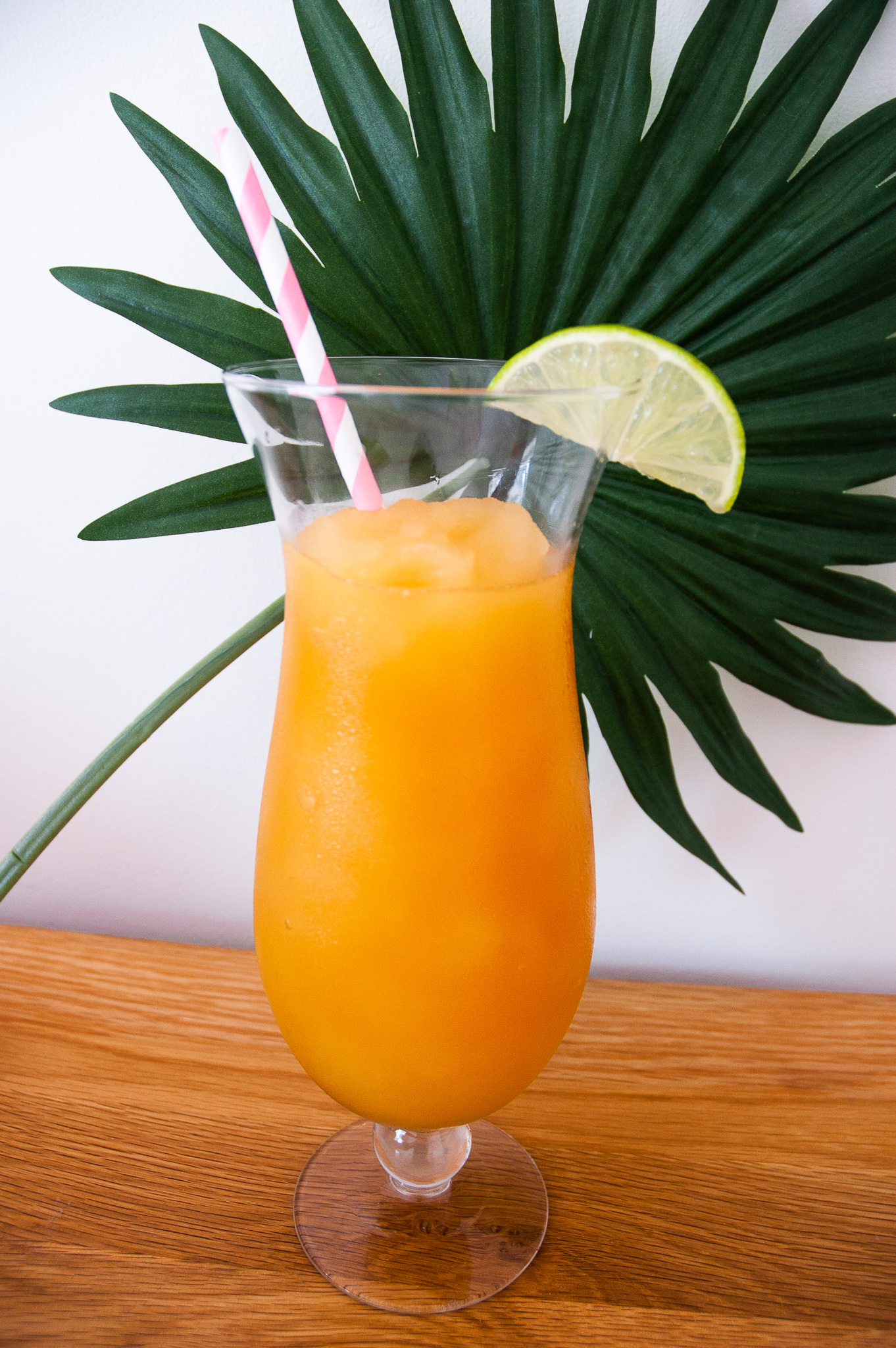 Pineapple and Orange Rum Slush in a tall glass in front of a palm leaf