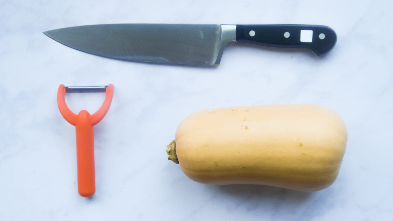 a peeler, a butternut squash and a chef's knife