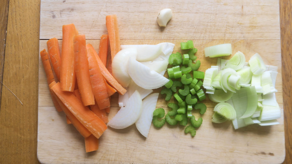 A chopping board with sliced carrots, onion, celery and leek