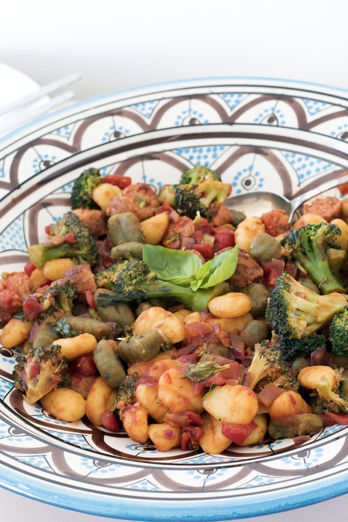 A blue patterned bowl with gnocchi, beans and basil leaves
