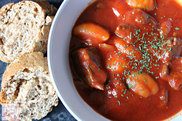 a white bowl with tomato sauce and gnocchi and bread on the side