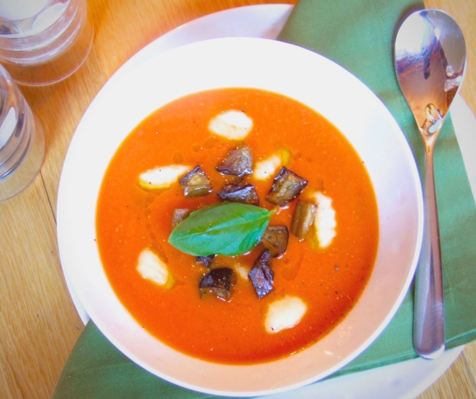 A white bowl full of tomato soup and gnocchi, topped with a basil leaf