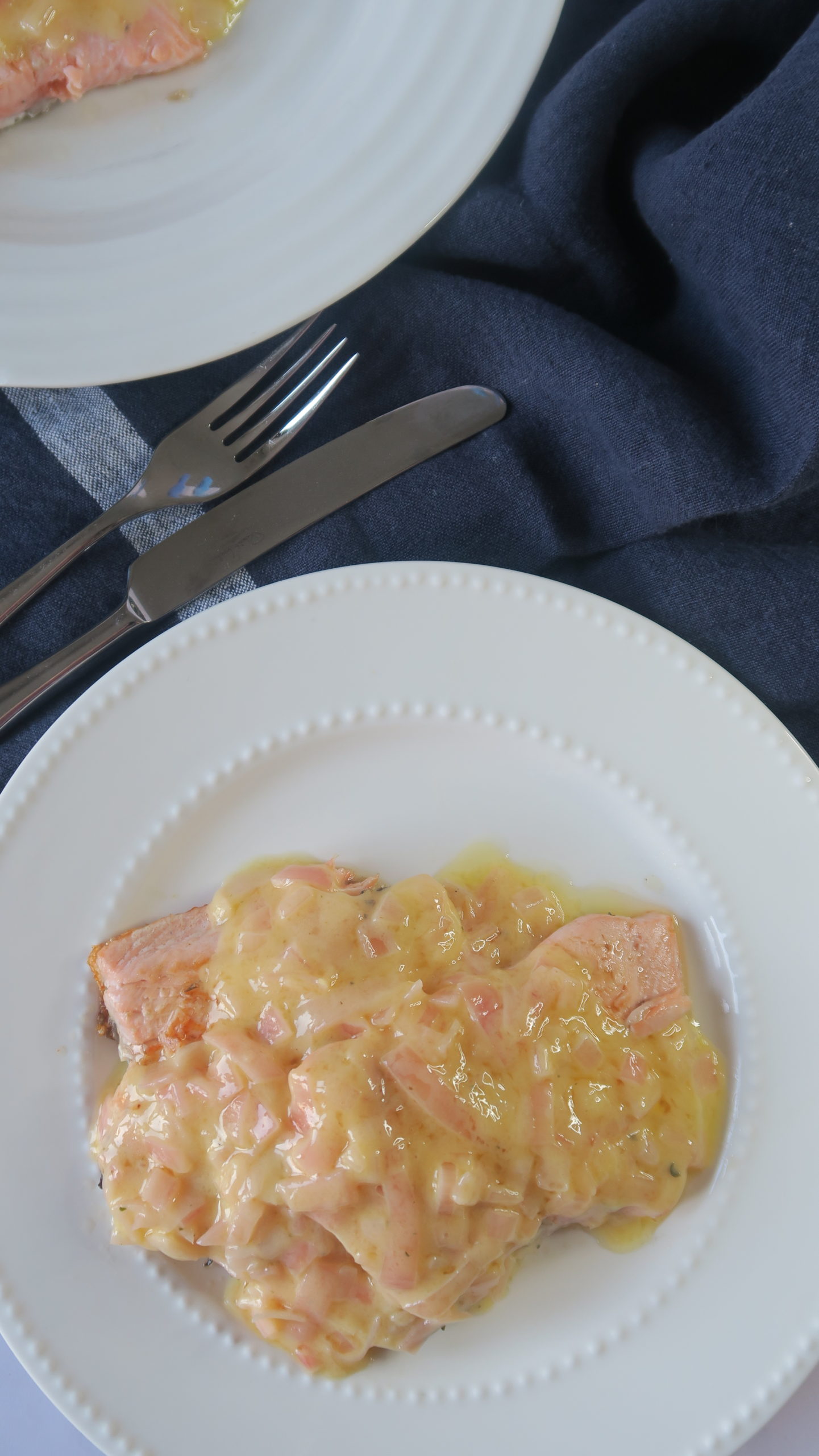 A white plate on top of navy linen with two pieces of salmon covered in creamy butter sauce