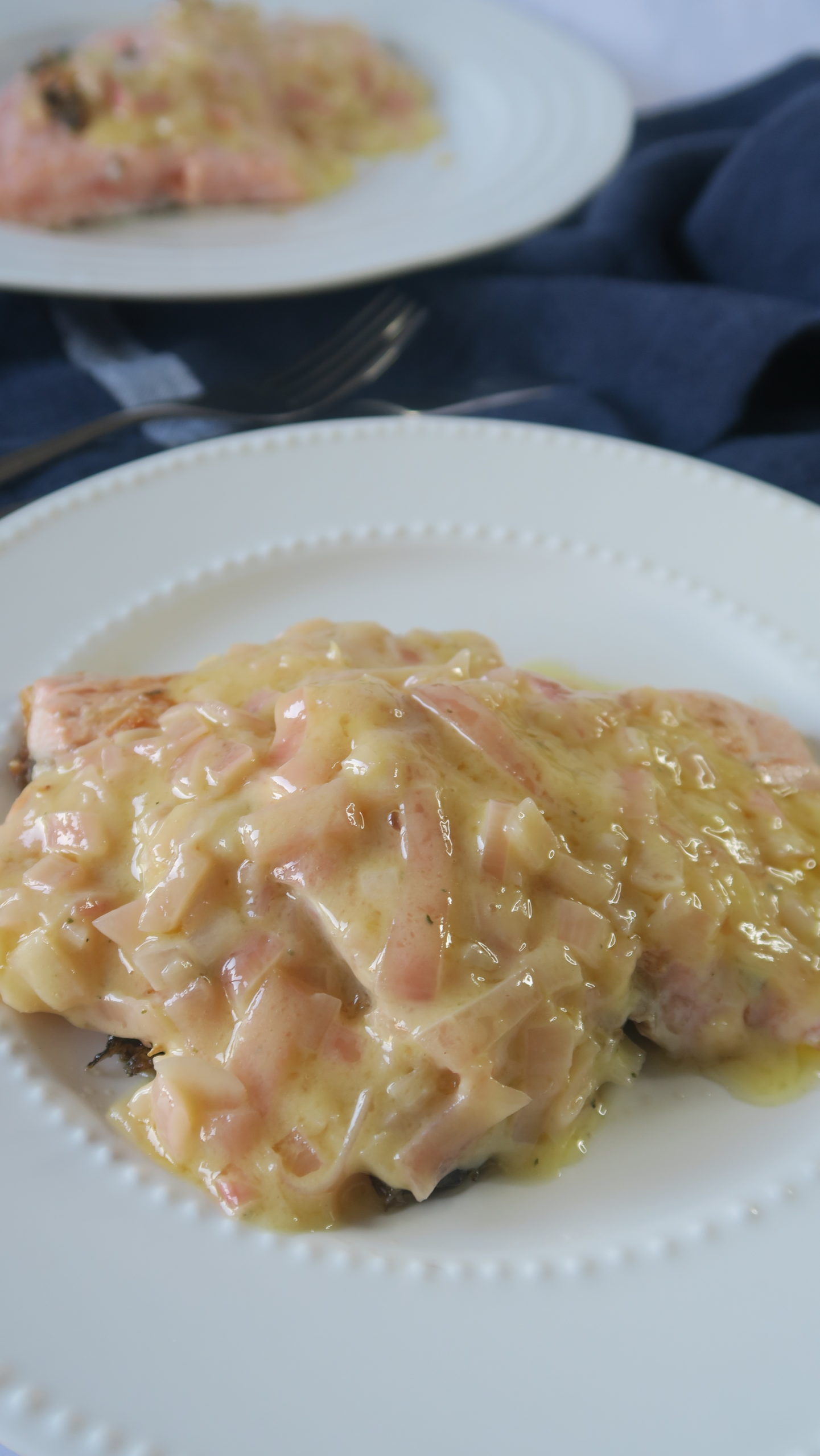 A white plate on top of navy linen with two pieces of salmon covered in creamy butter sauce