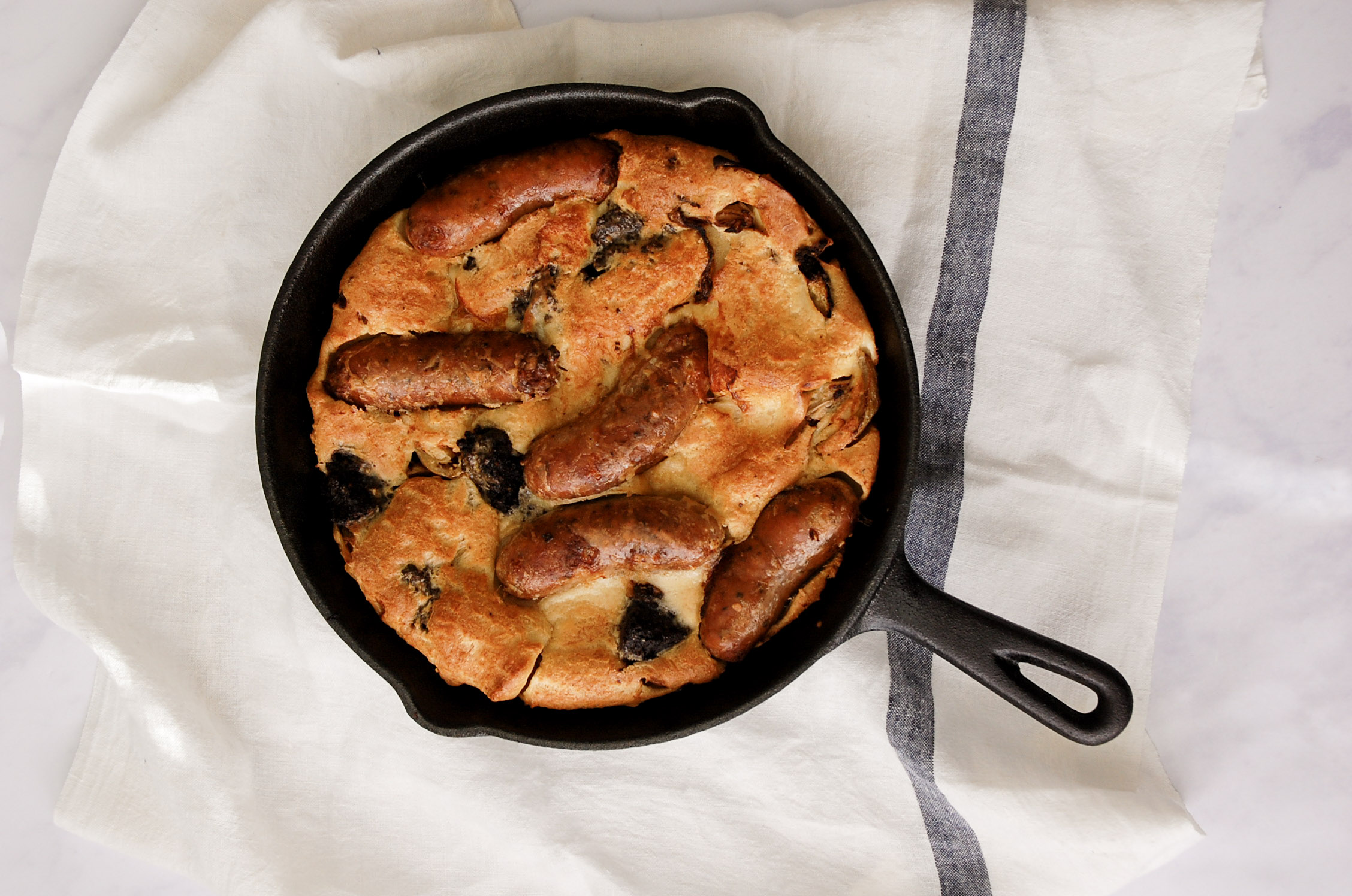 overhead shot of toad In the hole in a cast iron pan with white linen background