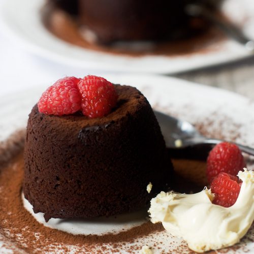 Chocolate fondant on a plate with cocoa dusting, raspberries and clotted cream