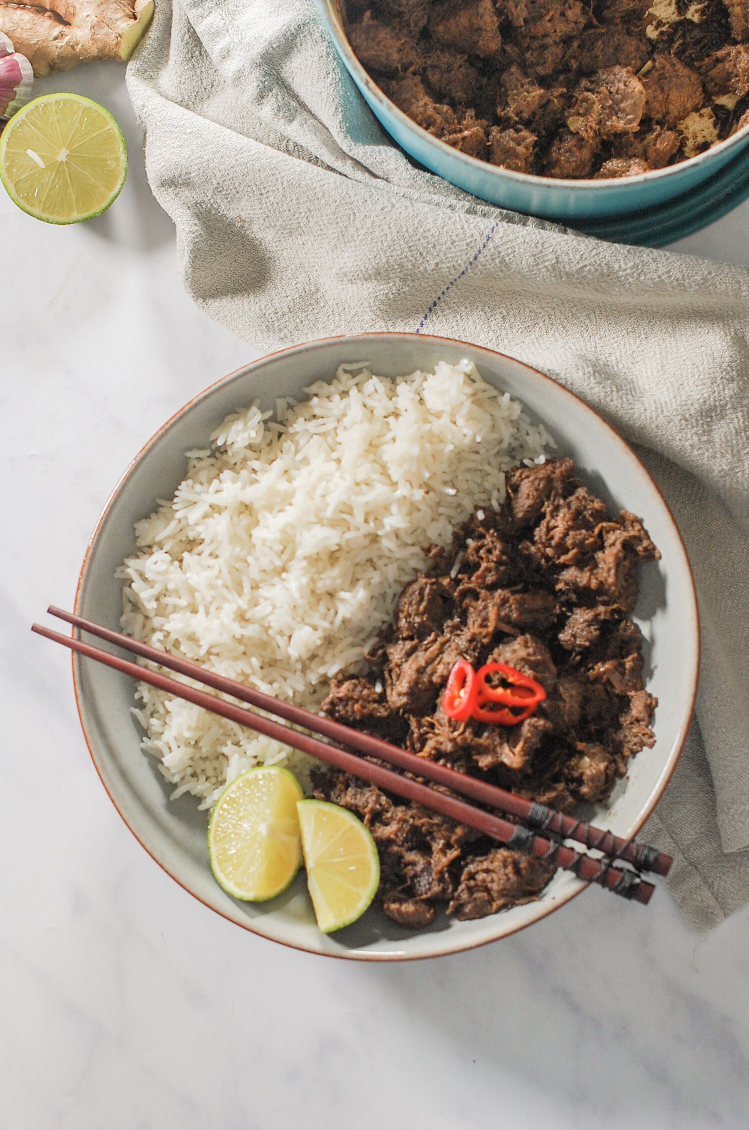 a bowl of Beef Rendang with rice, 2 lime slices and a pair of chopsticks.