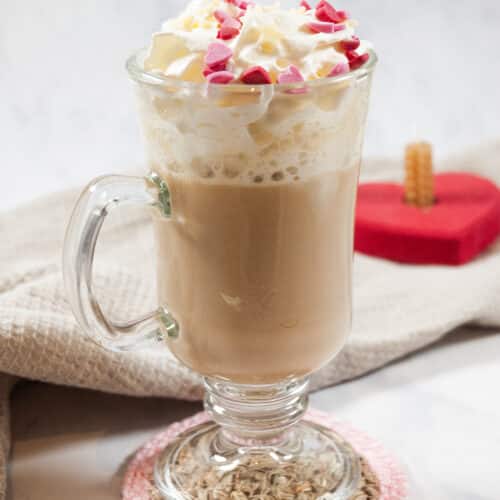 a clear glass filled with coffee, topped with whipped cream and little pink hearts.