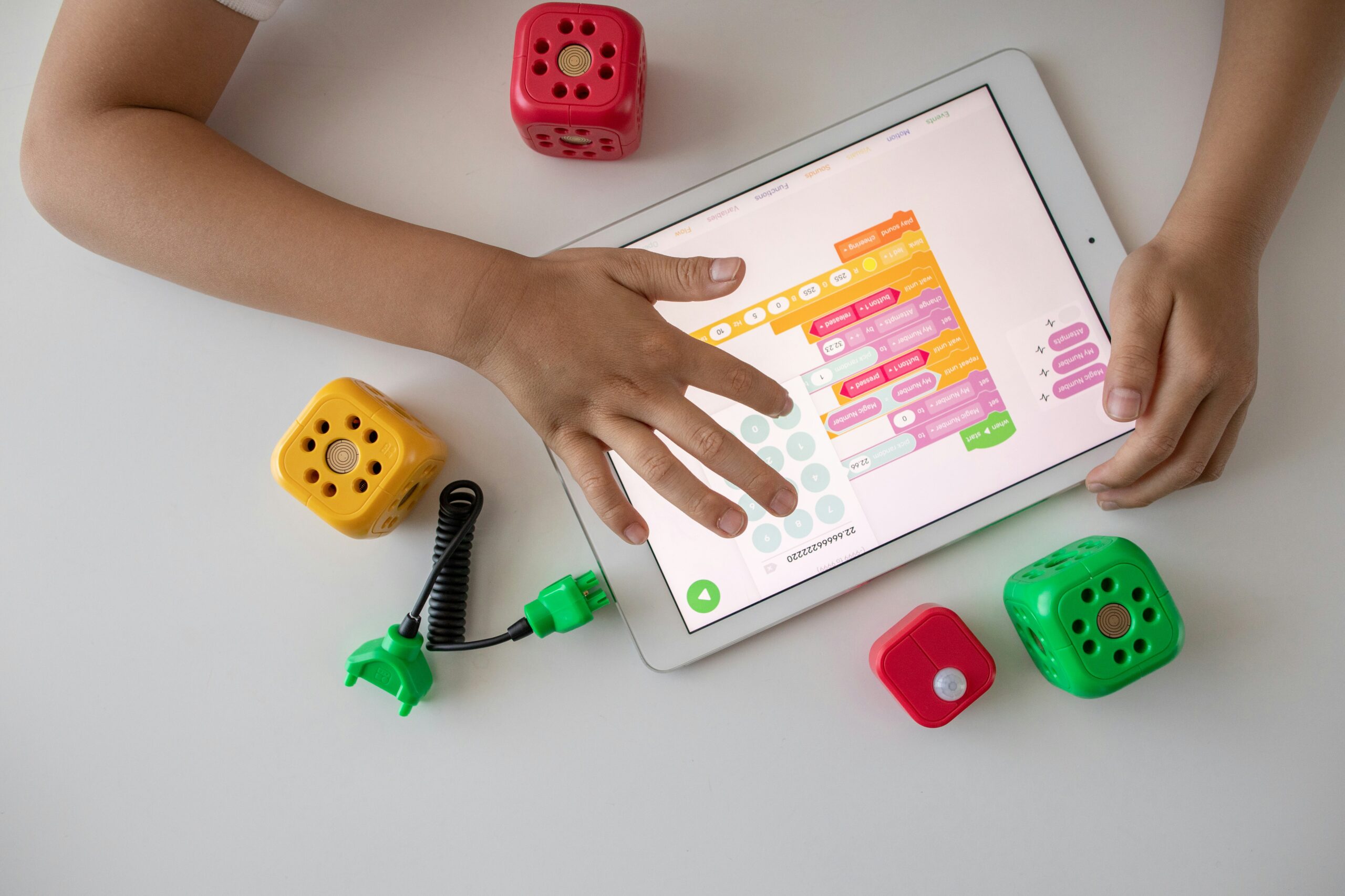 a birds eye view of some hands on an ipad which displays coding software for kids.
