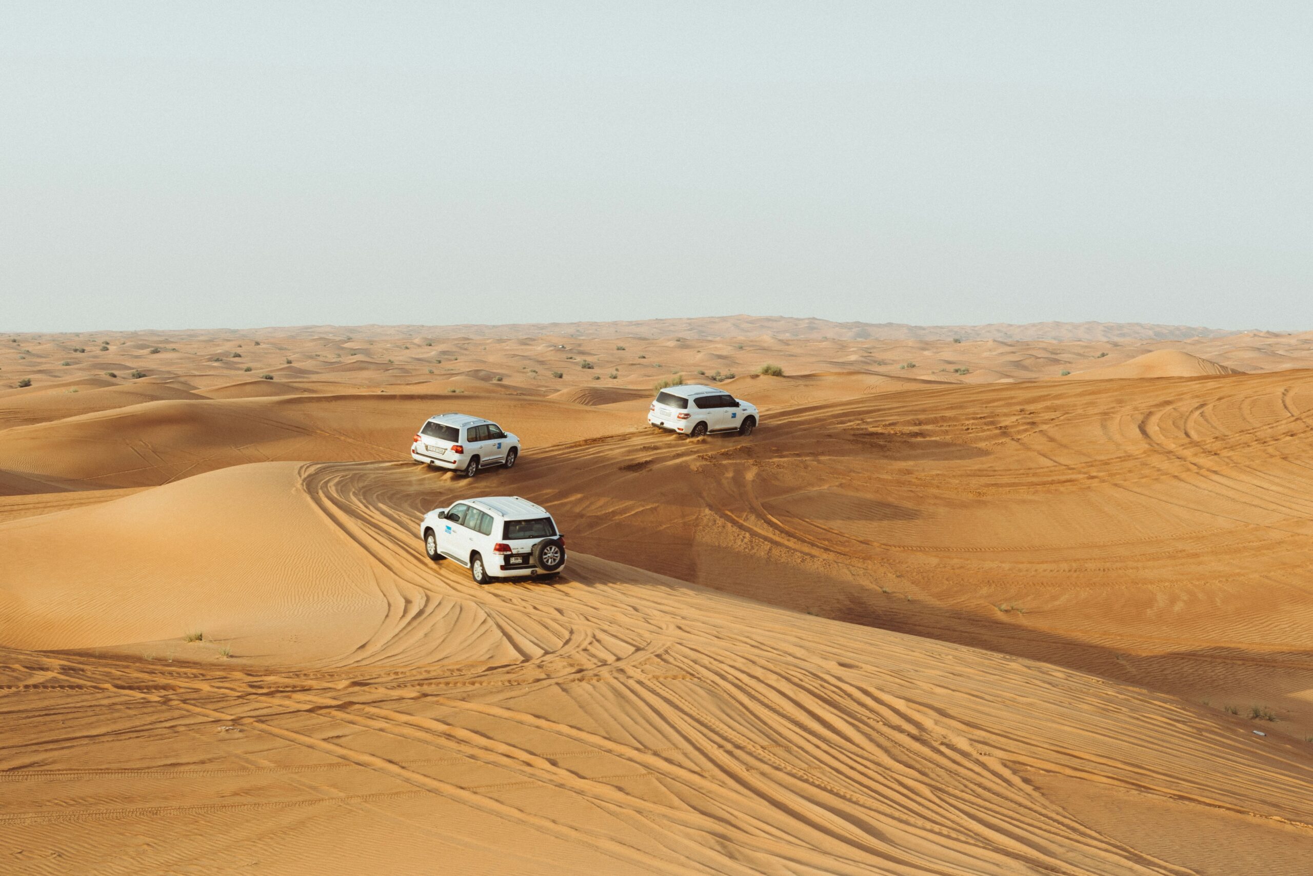 Three desert safari jeeps riding across the sand dunes