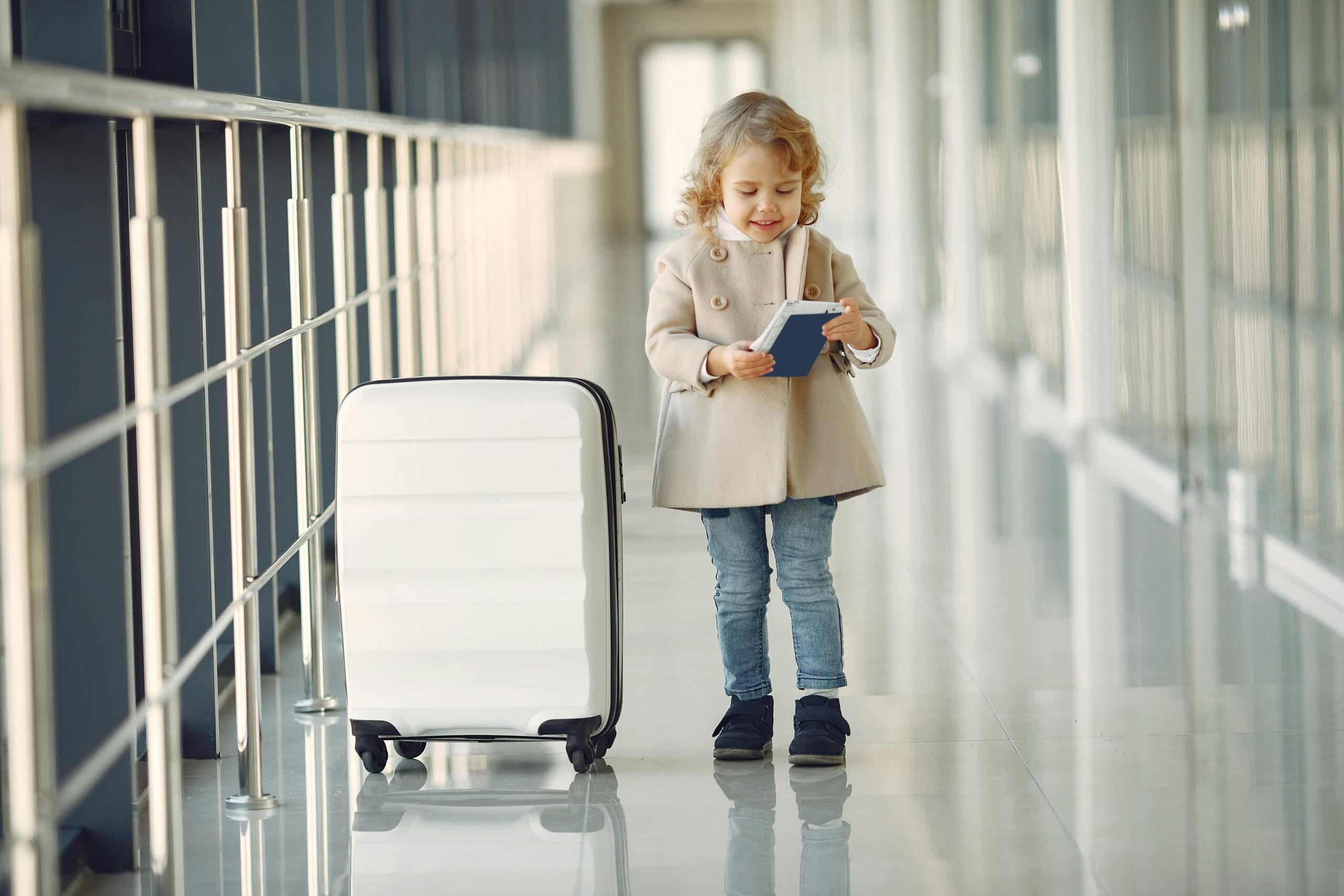 a happy little girl standing by a white suitcase